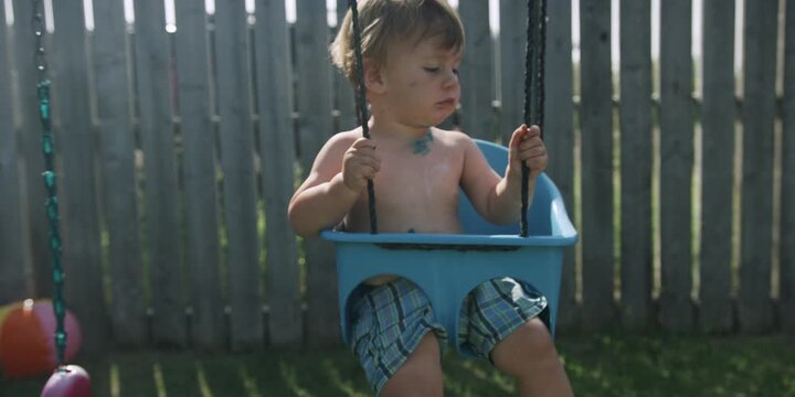 Toddler sitting in a swing holding onto the ropes