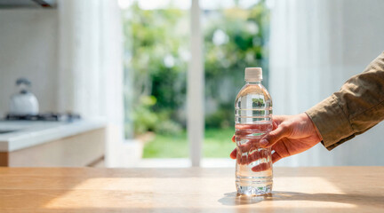 Hand reaching for a clear plastic water bottle on a wooden table. Hydration concept in a bright kitchen setting