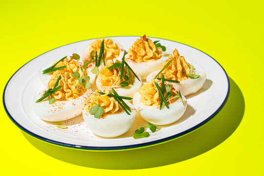 Deviled eggs served on a white plate with herbs on a bright yellow surface