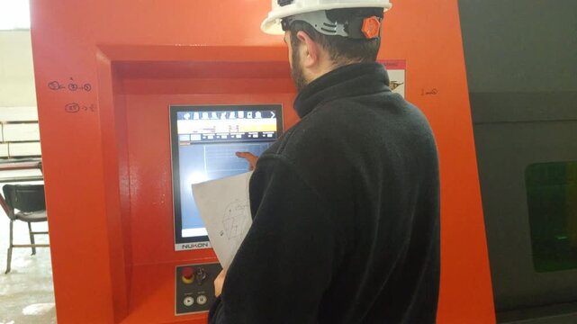 ​"A professional CNC operator wearing safety gear is seen configuring production details and technical parameters on a modern touch screen control panel before starting the industrial manufacturing pr