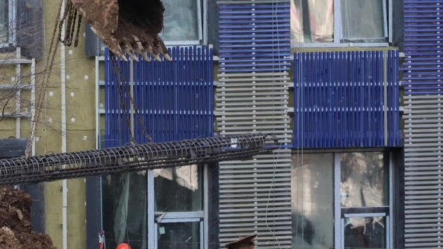 The excavator uses a bucket on metal chains to carry the metal mounting structure. 