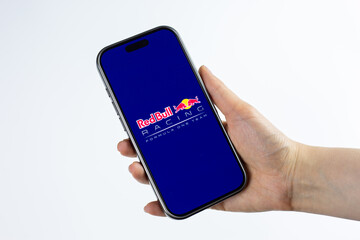 Fototapeta premium Moscow, Russia, March 14, 2026: Hand holding smartphone displaying Red Bull Racing Formula 1 Team logo on screen, isolated on white background. Edge technology and innovation in Formula 1 motorsport