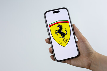 Fototapeta premium Moscow, Russia, March 14, 2026: Hand holding smartphone displaying Scuderia Ferrari shield logo with prancing horse and SF letters on screen. Legendary racing team heritage and motorsport tradition