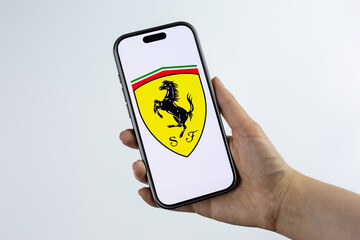 Fototapeta premium Moscow, Russia, March 14, 2026: Smartphone in hand showing Scuderia Ferrari shield logo with prancing horse on display, isolated. Formula 1 victories, podium finishes and championship spirit in race