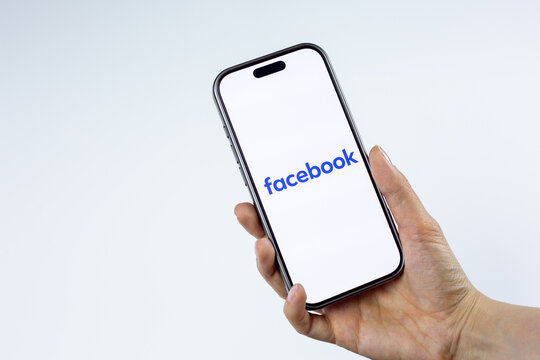 Moscow, Russia, March 14, 2026: Female hand holding smartphone displaying blue Facebook wordmark on screen, isolated on white background. Meta corporate branding and company news coverage