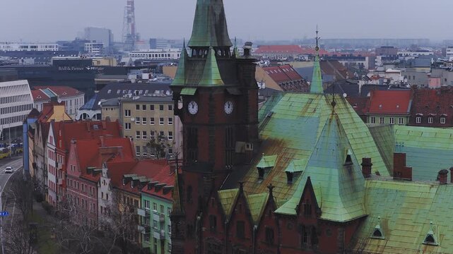 Aerial daytime pan of Wroclaw, Poland, centers on ornate clock tower, verdigris copper roofs, red tiled gables, tram tracks, slow cars and trams under overcast light.