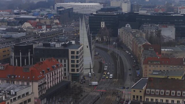 Aerial Wroclaw, Poland shows trams, buses, cars, and pedestrians on a curved multi lane street with tram tracks, a modern spire tower, Accenture block, and oval structure.