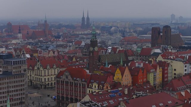 Aerial view over Wroclaw, Poland shows Rynek, Gothic clock tower, patterned roof tiles, vivid gabled townhouses, twin cathedral spires, and slow sweeping motion.