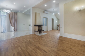 Naklejka premium A bright living area has a wooden floor and large windows. The room features a fireplace and an open layout leading to other spaces. Curtains are present on one side