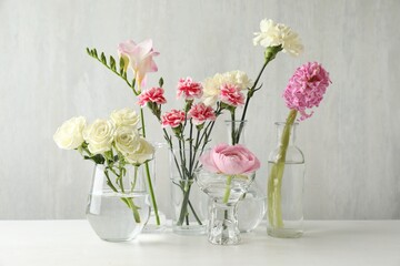 Fototapeta premium Different beautiful flowers in vases on light table indoors