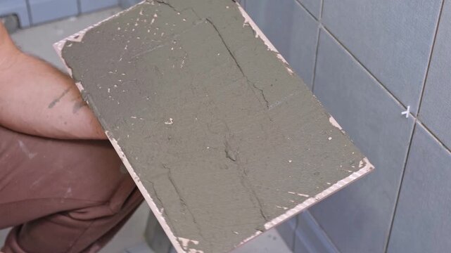 Tile adhesive spreading. Tiling mortar application. Worker smoothing adhesive. Workman smoothing grout on ceramic tiles. Bathroom renovation. Man using notched trowel, cement spread across tile back