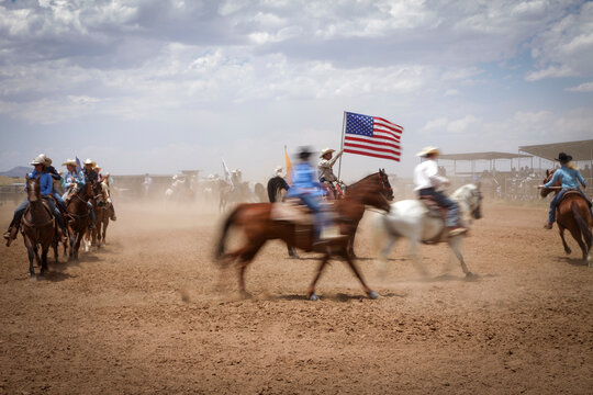Galisteo, New Mexico, United States. Rodeo riders carrying American flag during western rodeo event. Motion blur