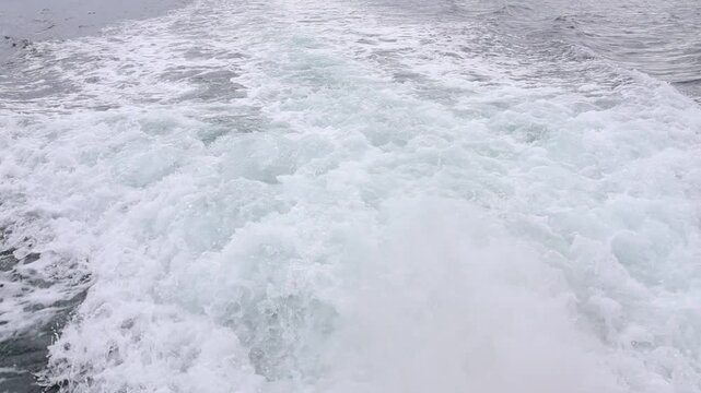 Seawater being agitated by a boat's engine forming a white foam; the engine smoke can be subtly noticed.