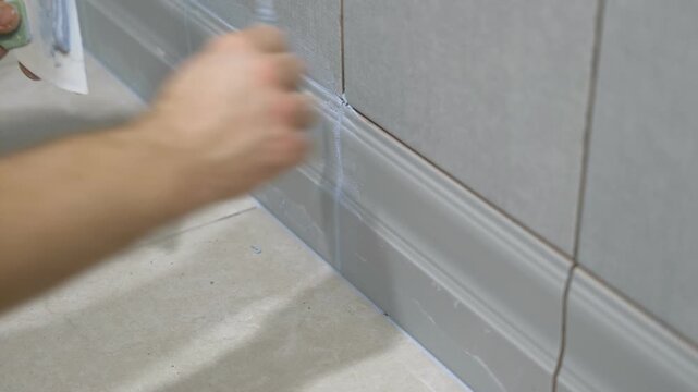Worker using a rubber grout float to smooth grout between tiles. Carefully applying sealant to tiles joints. Workman hands smoothing caulk, using small tool to remove excess and create clean seam.