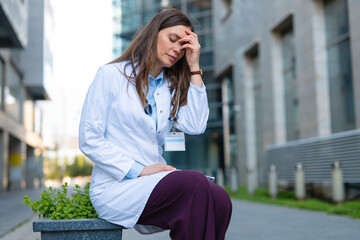 Fototapeta premium Stressed female doctor feeling headache and burnout outdoors