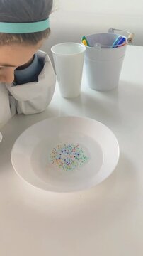 Time-lapse style shot of colorful ink dots dissolving and spreading in a bowl of water, demonstrating solubility and diffusion.