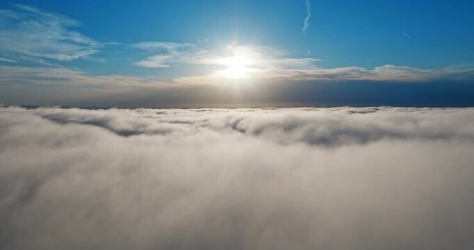 Cinematic drone view soaring over white clouds blanket towards radiant sun. Heavenly atmospheric landscape high altitude flight. Success future vision hope inspiration concept aerial