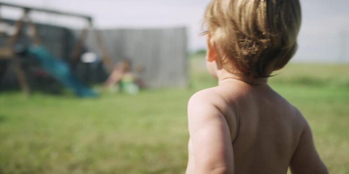 Toddler walking in a backyard facing away from camera