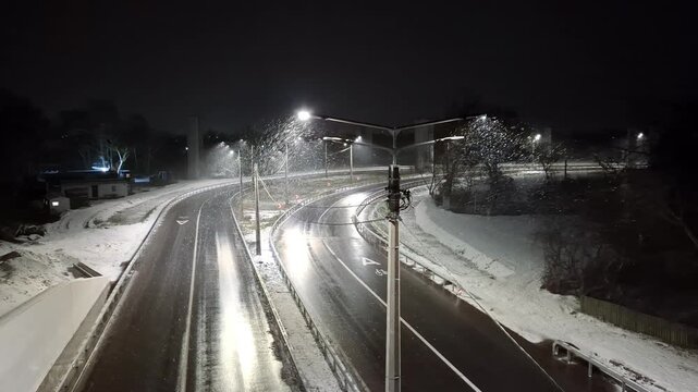 Winter night, and the road is empty of cars, with snow falling on the roadway