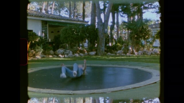 A child is captured jumping high on an in-ground trampoline in a backyard setting on super 8 film