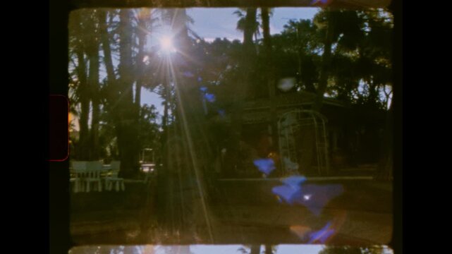 A low angle view of a child captured mid-motion jumping high on an in-ground trampoline with lens flare on analog super 8 film