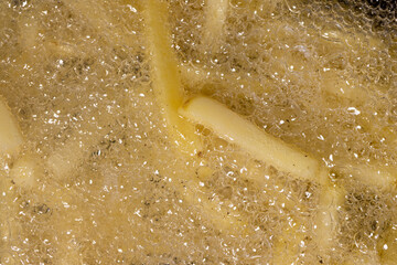 overcooked orange French fries in sunflower oil during frying in a frying pan, delicious fast food...