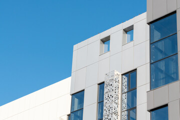 Obraz premium Modern architectural building facade featuring large glass windows and decorative panel against a clear blue sky, showcasing contemporary design elements and materials