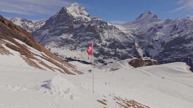 Breathtaking winter scenery: Swiss flag fluttering in front of massive snowy mountain peaks.