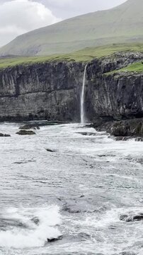 Green nordic landscapes of the Faroe Islands. Molin waterfall flowing down from cliffs into the Atlantic Ocean amidst greenery, Eysturoy island.