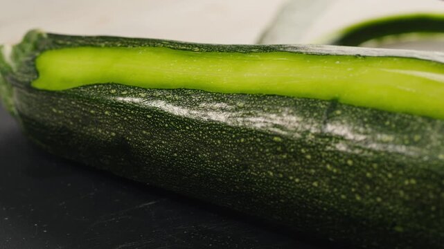 Young green zucchini are cut with a knife on a wooden board on the table. 