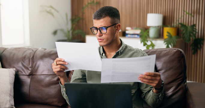 Man, reading and documents with laptop in home for finanial planning, audit or investment on sofa. Male person, checking and paperwork with insurance on computer for budget, finance bills or expenses