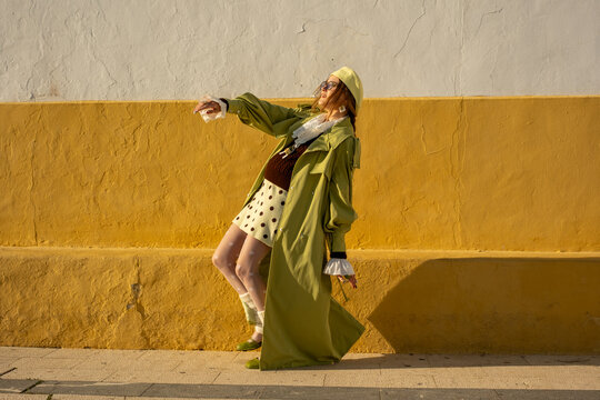 Fashionable woman posing against a bold yellow wall in trendy retro outfit and accessories