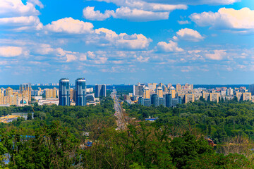 Panoramic view of a sprawling Eastern European city skyline with lush green trees in the foreground