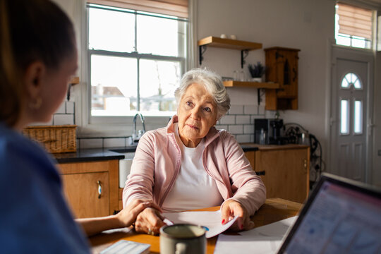 Senior woman reviewing paperwork with caregiver at home kitchen