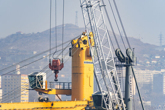 Vladivostok, Russia - February 15, 2026: Liebherr crane with red hook and cables against a backdrop of buildings and hills in an industrial setting