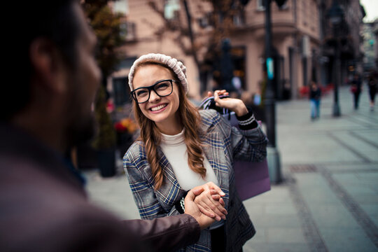 Smiling young woman with shopping bags holding hands on city street