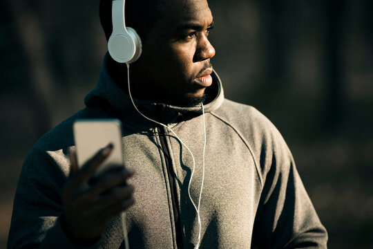 Man with wired headphones holding smartphone outdoors