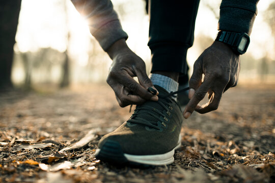Runner tying shoelaces on forest trail at sunrise