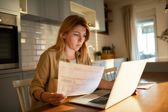 Concerned woman reviewing bills on laptop at kitchen table