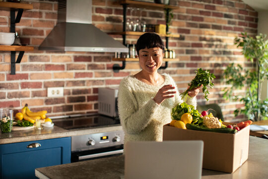 Smiling woman unboxing fresh groceries in home kitchen