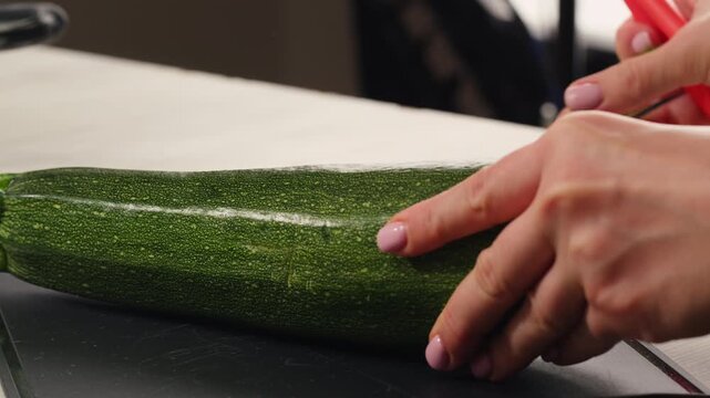 Young green zucchini are cut with a knife on a wooden board on the table. 