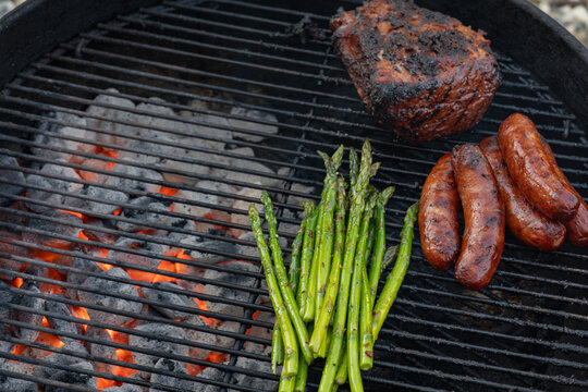 Steak, sausages, and fresh asparagus on a charcoal grill