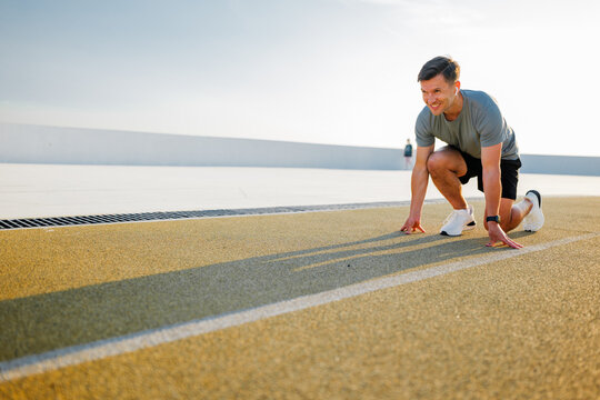 Runner in starting position on an outdoor track prepares for a sprint with a determined smile under the morning sun