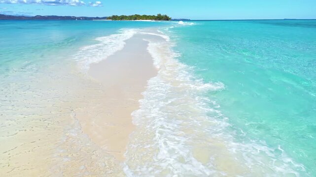 Aerial drone view above a long white sandbar surrounded by crystal clear turquoise ocean water, leading toward a small tropical island in Madagascar