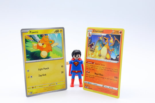 Superman toy holding two Pokemon cards. Pawmi and Charizard. Concept photo.