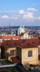 Obraz premium St Nicholas Church crowns Prague skyline above red tile rooftops under blue sky