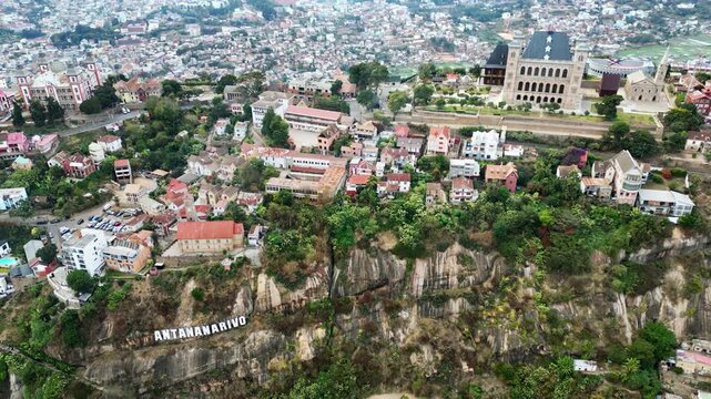 Aerial drone view above Antananarivo with the city skyline spread across surrounding hills, showing dense urban neighborhoods and the large historic palace complex overlooking Madagascar's capital