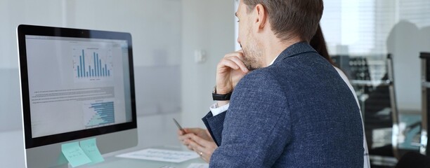Obraz premium Business colleagues analyzing financial data on computer, discussing project statistics and market trends in office meeting. Businesspeople concept
