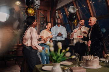 Diverse friends laughing and dancing during birthday celebration at a decorated loft party with...