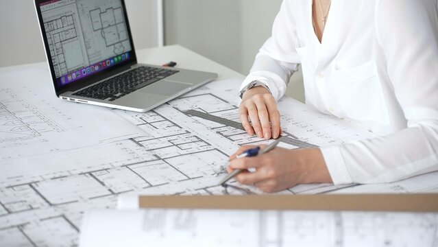 Architect working on building blueprint plans, designing new residential or commercial real estate projects for construction, using a ruler and laptop on a desk